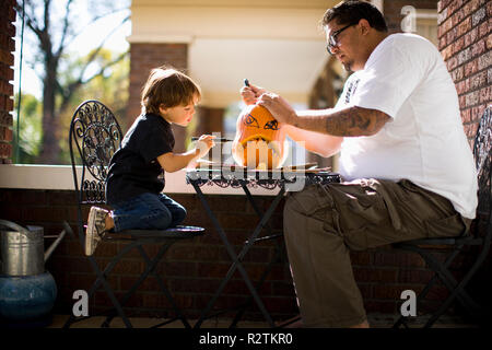 Père et fils s'appuyant sur la face et la sculpture de citrouille Jack O' Lantern Banque D'Images