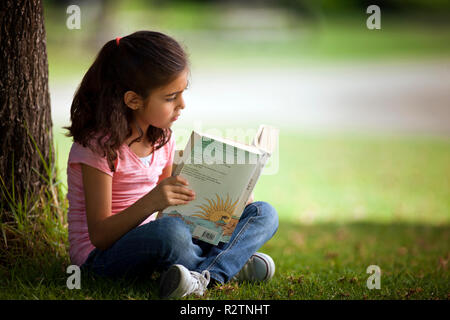 Fille assise seule à l'extérieur tout en lisant un livre. Banque D'Images