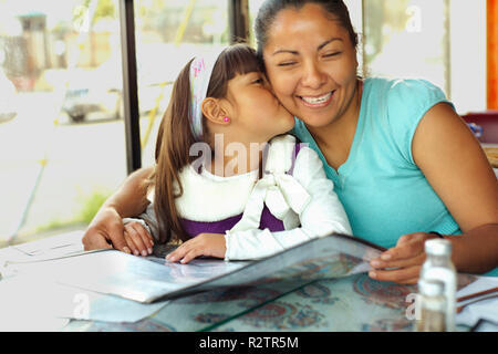 Jeune fille, l'embrasse sur la joue de la mère pendant qu'elle regarde une carte de restaurant. Banque D'Images