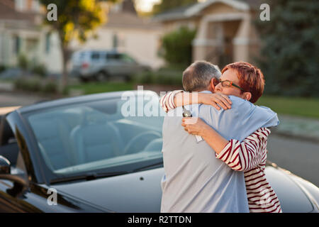 Smiling woman hugging devant leur nouvelle voiture. Banque D'Images