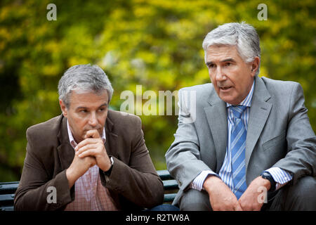 Deux hommes d'âge mûr parler sérieusement, assis ensemble sur un banc de parc. Banque D'Images