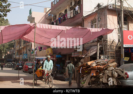 New Delhi, Inde - Le 11 janvier 2015 : rue de la ville avec maisons et commerces panneaux. Rickshaw Man dans un turban traditionnel transporte des passagers. Banque D'Images