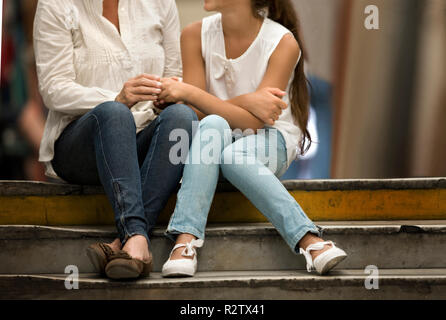 Jeune fille assise sur l'escalier à l'intérieur d'un centre commercial avec sa mère. Banque D'Images