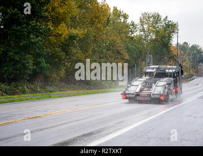 Gros camion vide puissant transporteur voiture foncé semi truck chargement de voitures sur deux niveaux de la conduite d'un semi-remorque sur la route mouillée glissante sous la pluie wit Banque D'Images