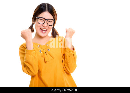 Studio shot of young happy Asian woman cheering avec les deux bras r Banque D'Images