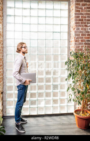 Portrait of a young caucasian businessman habillé en passant près du mur avec des briques de verre à l'intérieur Banque D'Images