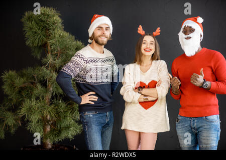 Jeunes amis vêtus de chandails avec de nouveaux chapeaux année célébrant l'hiver vacances ensemble à l'intérieur Banque D'Images