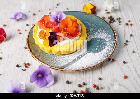 Tarte aux fraises garnies de fleurs comestibles sur une plaque bleue Banque D'Images