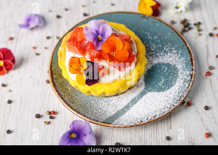 Tarte aux fraises garnies de fleurs comestibles sur une plaque bleue Banque D'Images