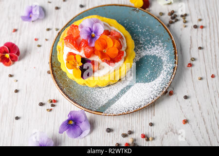 Tarte aux fraises garnies de fleurs comestibles sur une plaque bleue Banque D'Images