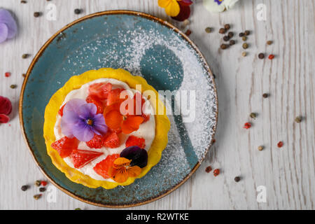 Tarte aux fraises garnies de fleurs comestibles sur une plaque bleue Banque D'Images