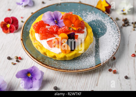 Tarte aux fraises garnies de fleurs comestibles sur une plaque bleue Banque D'Images