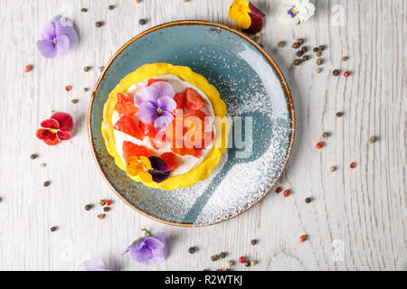 Tarte aux fraises garnies de fleurs comestibles sur une plaque bleue Banque D'Images