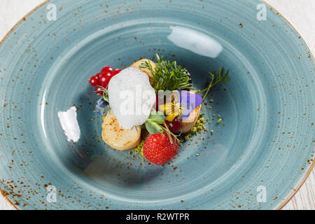 Poires poêlées sur un lit de pistaches au sol, garni de mousse d'oeufs sur une plaque bleue Banque D'Images