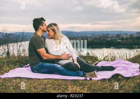 Heureux mari embrasser sa femme enceinte en front et profiter de passer du temps ensemble à l'extérieur. Banque D'Images