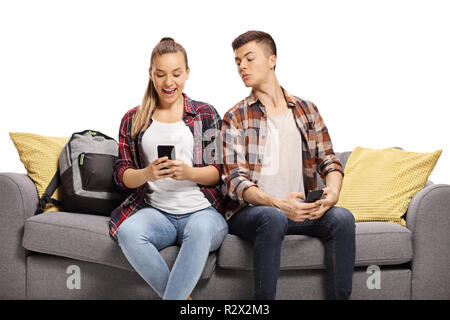 Teenage boy regarder le téléphone d'une adolescente assise à côté de lui sur un canapé isolé sur fond blanc Banque D'Images