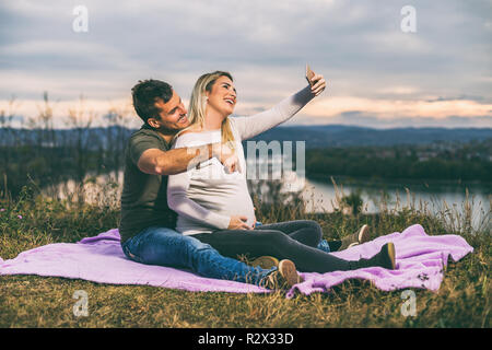 Heureux mari et sa femme enceinte en tenant pendant qu'ils selfies aiment passer du temps ensemble à l'extérieur. Banque D'Images