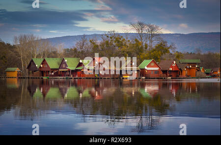 Tata, Hongrie - chalets de pêche par le lac Derito sur une petite île au coucher du soleil avec des réflexions et coloré Ciel et nuages Banque D'Images