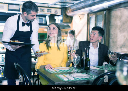 L'homme est chef de l'ordre apporte au couple qui avons le dîner et boire du vin dans un restaurant. Banque D'Images