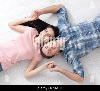 Jeune couple sympathique, gisant sur le sol, se regarder et rêver de mobilier pour le nouvel appartement. Maquette pour la conception. Banque D'Images