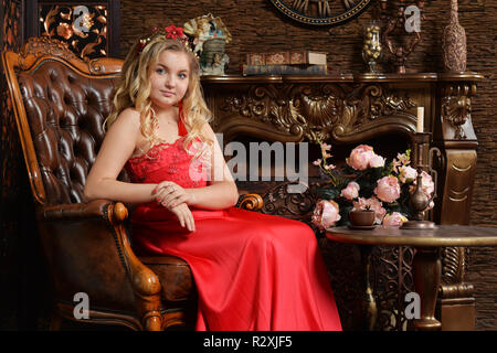 Adolescente blonde en robe rouge vif sitting in armchair Banque D'Images