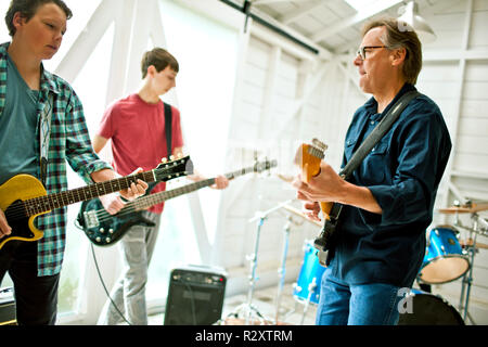 Mid adult man et deux adolescents joueurs de guitare ensemble à l'intérieur d'un garage. Banque D'Images