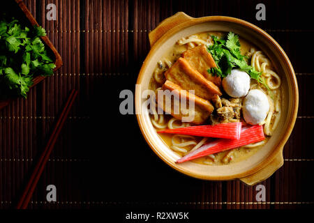 De savoureux fruits de mer épicés soupe laksa avec du pain, du crabe, des nouilles sur fond bambou Vue de dessus Banque D'Images