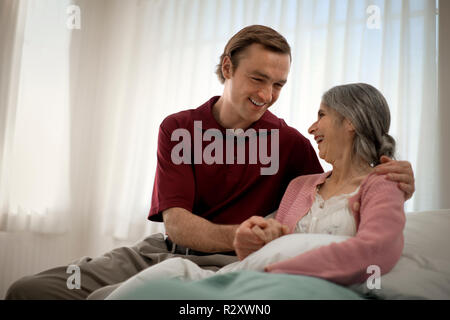 Infirmier rire réconfortant une vieille femme à son chevet. Banque D'Images