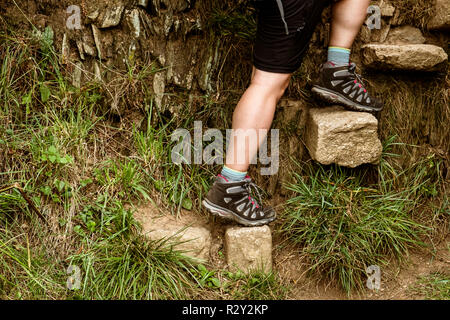 Un homme grimper une série de pierres encastré dans un mur création d'étapes sur un chemin côtier. Banque D'Images