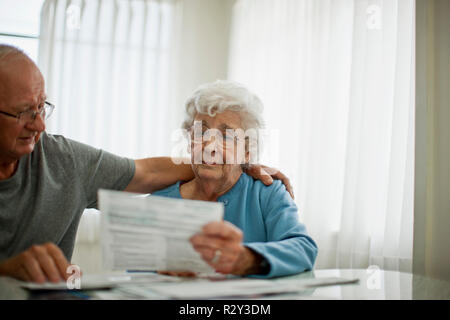 Couple de personnes âgées anxieux essaient de réconforter les uns les autres comme ils s'inquiètent d'un projet de loi qu'ils ont reçues. Banque D'Images