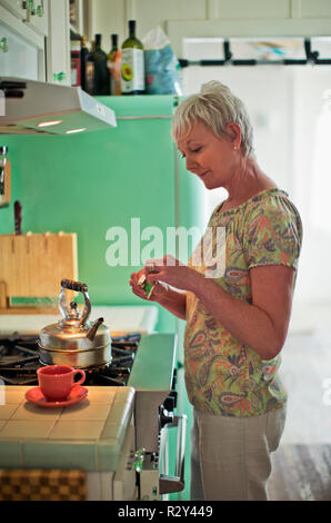 Femme mature préparer une tasse de thé dans sa cuisine. Banque D'Images