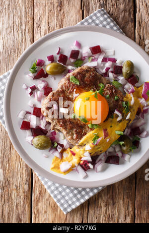 Tartare de boeuf frites ou Steak Parisien - Pariserbof avec des œufs, des légumes et de la moutarde gros plan sur une assiette sur la table. Haut Vertical Vue de dessus Banque D'Images