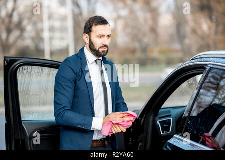 Elegant businessman dans l'action de frotter les mains avec un chiffon doux après le lavage de voiture en libre service station Banque D'Images