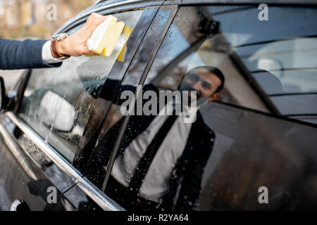 Businessman lave-vitre de voiture avec une éponge et de la mousse sur un self service lavage de voiture, près d'une réflexion sur la fenêtre Banque D'Images