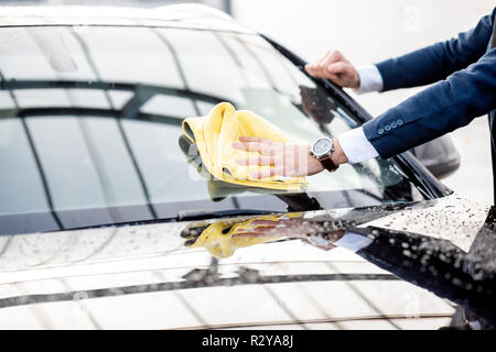 Businessman vêtu d'un costume d'essuyer le pare-brise de sa voiture avec du jaune sur une microfibre lavage de voiture en libre service, close-up view avec pas de visage Banque D'Images