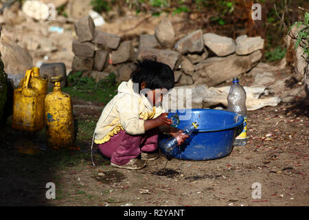 Jeune enfant autochtone jouant avec une bouteille en plastique, un bol en plastique bleu et de l'eau dans un village rural andin, Bolivie Banque D'Images