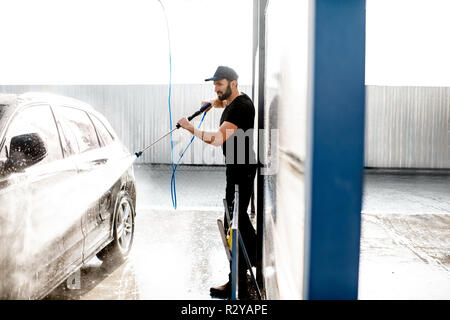 Rondelle professionnel en uniforme noir lave-voiture de luxe avec canon à eau sur un lavage de voiture en plein air Banque D'Images