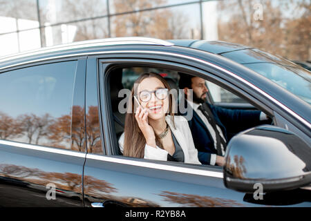 Portrait élégant téléphone avec voiture de luxe avec la conduite d'affaires dans la ville, vue de l'extérieur à travers la fenêtre Banque D'Images