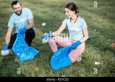 Heureux l'homme et la femme bénévoles vêtus de t-shirts bleus jardin public de nettoyage dans les sacs poubelles en plastique Banque D'Images