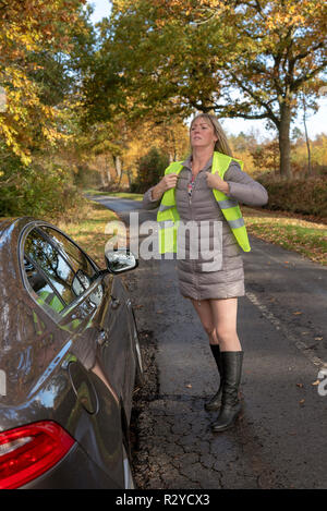 Automobiliste femme par sa voiture en mettant sur une veste de sécurité réfléchissante Banque D'Images