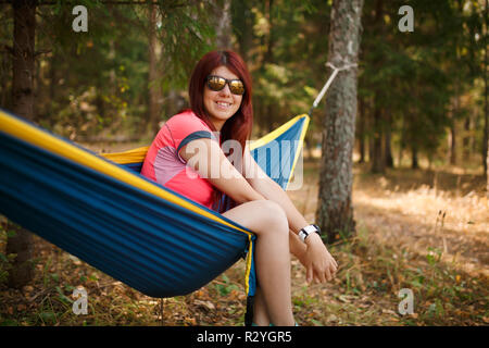 Photo de brunette à lunettes avec laptop sitting in hammock sur fond de forêt Banque D'Images