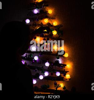 Arbre de Noël de branches pend sur le mur décoré avec des jouets et une orange et violet garland et la jeune fille tient une bougie allumée dans sa Banque D'Images