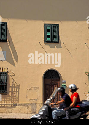 Flou de l'homme & femme en trombe, scooter le long de rue en face de l'immeuble typique de Florence avec des volets verts au centre de la ville,Toscane,Italie Banque D'Images