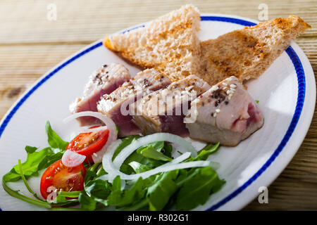 Délicieux thon frit légèrement saupoudré de sésame servi sur une assiette avec du pain grillé, tomates fraîches et vertes. Banque D'Images