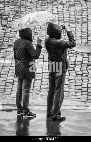 Les touristes à la pluie sur la Place Rouge, Moscou, Russie. L'homme et la femme portant des imperméables, holding umbrella tout en prenant une photo. Banque D'Images