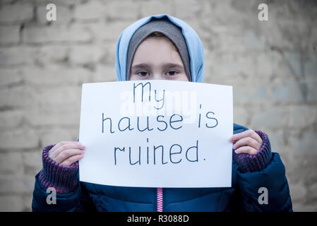 Fille de réfugiés avec une inscription sur une feuille blanche 'my house est ruiné' Banque D'Images