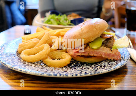 Un repas hamburger JD Wethercuillers Ultimate servi avec des rondelles d'oignon et des frites. Le repas est servi sur une table de pub dans un pub animé de Wethercuillers Banque D'Images