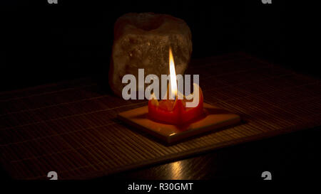 La flamme d'une bougie rouge allume le sel de pierre plateau lumière lampe sur sur un tapis de bambou avec fond noir. Banque D'Images