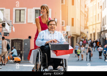 L'homme en fauteuil roulant qui est poussé par son ami sur un voyage de shopping Banque D'Images