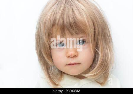 Blonde aux yeux bleus de bébé avec Bob et cheveux nez rayé close-up. Isolé sur blanc. Enfant de sexe féminin à la caméra au sérieux en fronçant les sourcils, studio blanc. Les émotions négatives, mécontentement, à l'infraction. Banque D'Images